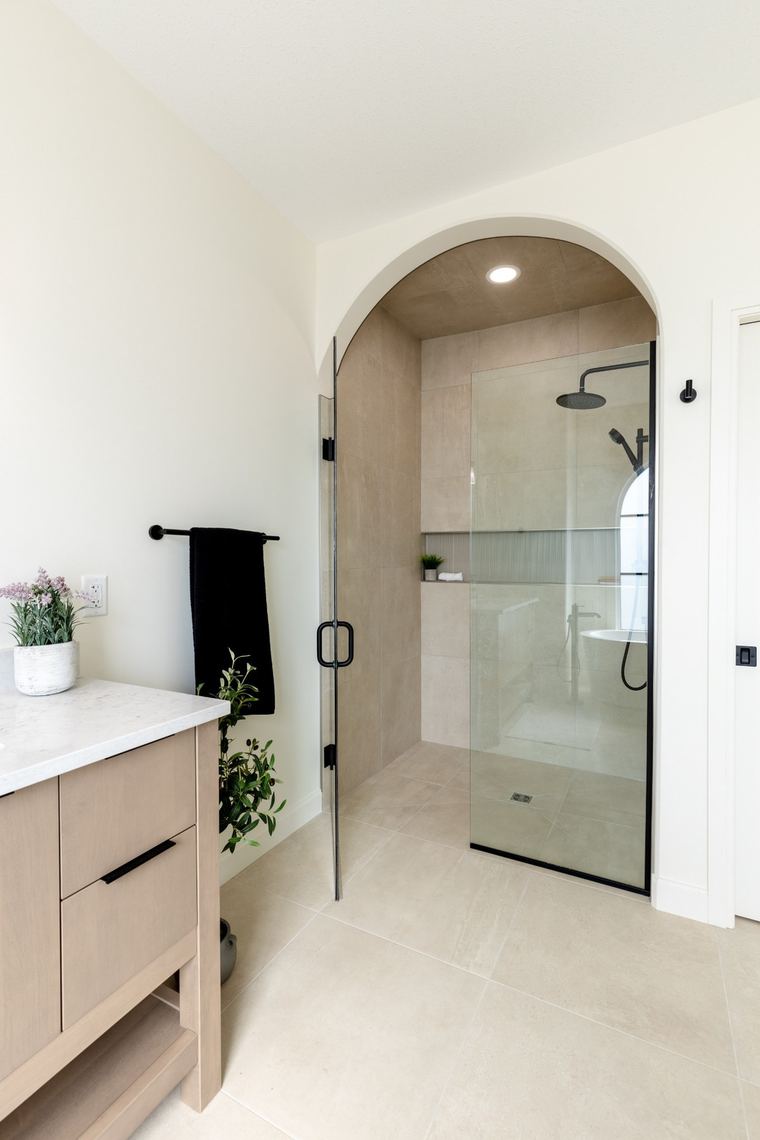 Spa-inspired walk-in shower framed by a custom arch, with frameless glass, neutral tile and matte black fixtures.