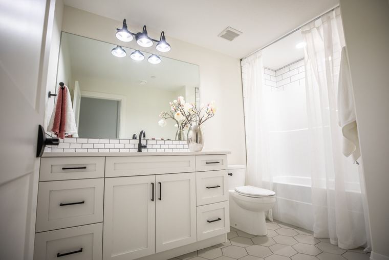 Bright basement bathroom with a white vanity, black hardware, hexagon tile flooring and a full tub-shower.