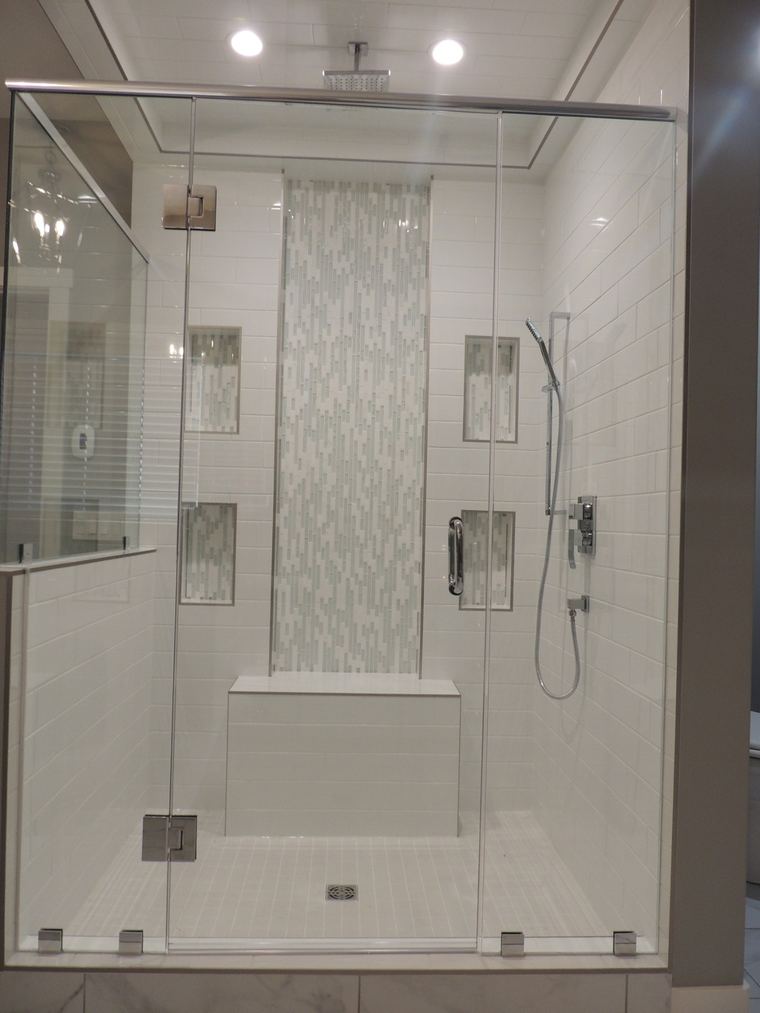 Custom walk-in shower with a built-in bench, rain head, handheld fixture, recessed niches and a full-height mosaic tile feature.