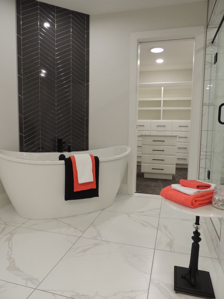 Primary ensuite with a freestanding tub, black herringbone tile feature wall and direct access to a custom walk-in closet.
