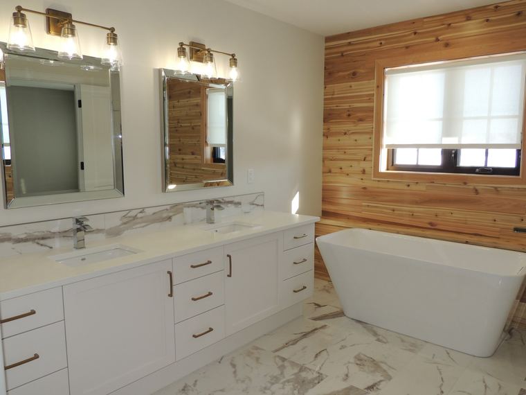 Primary ensuite with a double vanity, freestanding tub, warm wood feature wall and marble-look tile finishes.