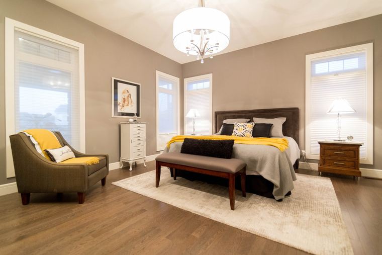 Spacious primary bedroom with hardwood flooring, multiple windows, a statement ceiling light and warm yellow accents.