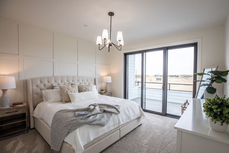 Bright primary suite with a panelled feature wall, upholstered bed, contemporary lighting and direct balcony access.