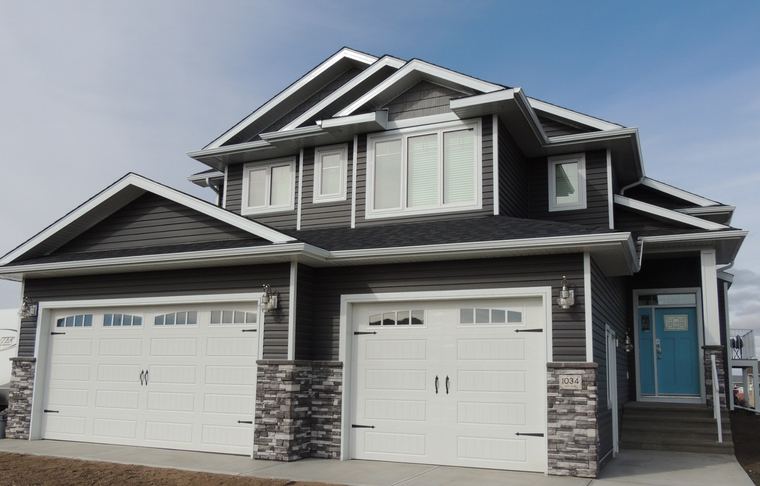 Dark siding two-storey family home with contrasting garage doors and stone accents.