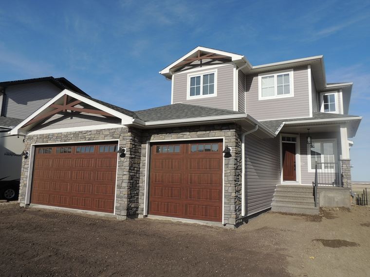 Grey two-storey family home with a triple garage, stone accents and timber gable details.