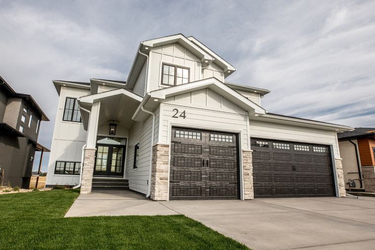 Modern white farmhouse exterior with black windows, stone accents and a three-car garage.