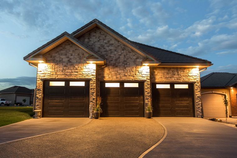 Stone-clad custom bungalow with a three-car garage and integrated architectural lighting.