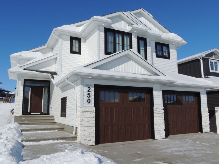 White modern farmhouse exterior with dark wood garage doors in a winter setting.