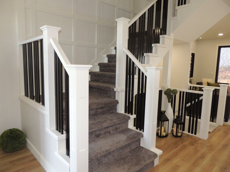 Carpeted staircase with black balusters, substantial white newel posts and a detailed panelled feature wall.