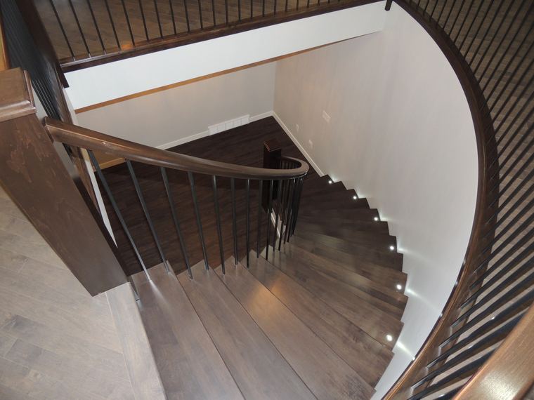 Curved dark wood staircase with black metal balusters, a sweeping handrail and integrated step lighting.