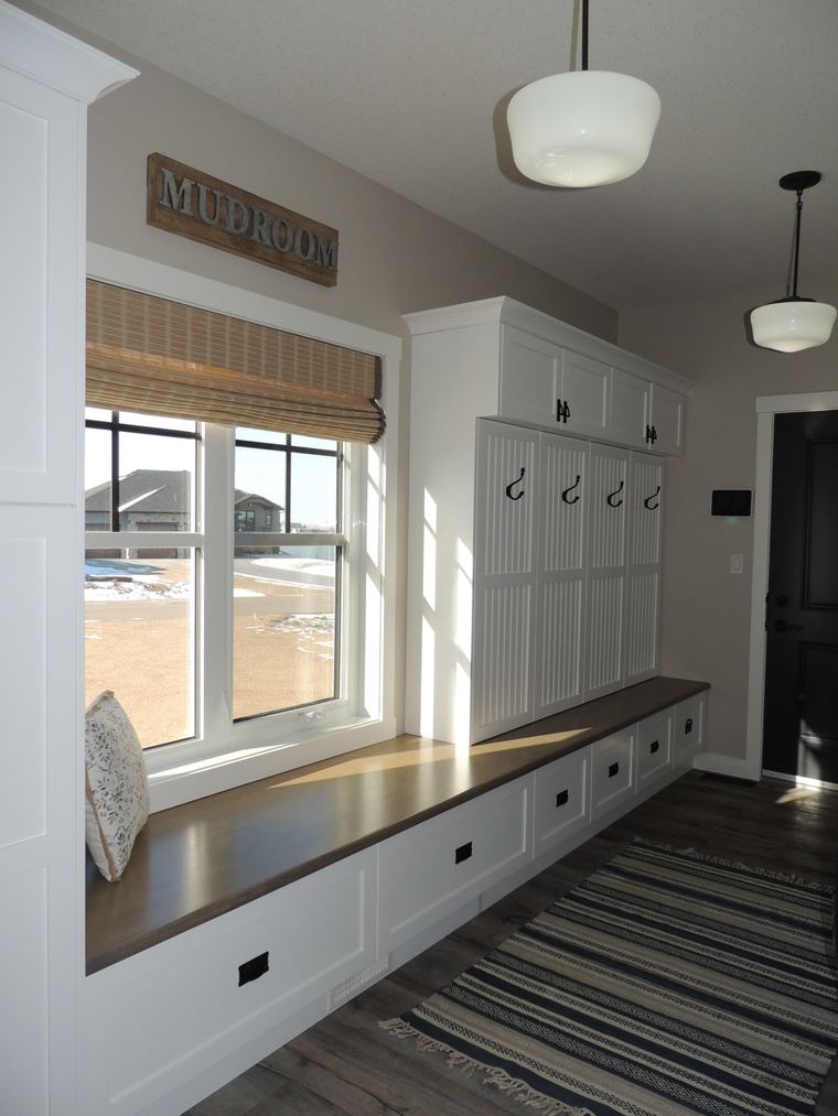 Custom mudroom with a long wood bench, coat hooks, overhead cabinetry, integrated drawers and natural light from a large window.