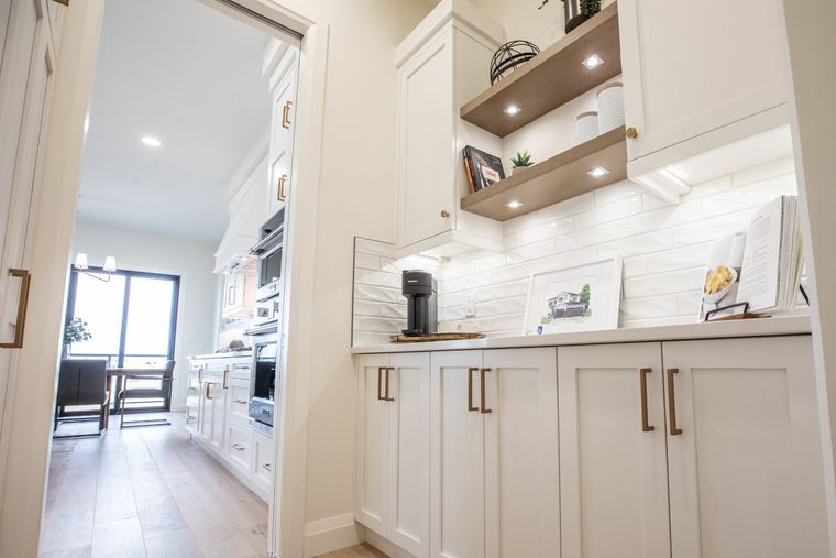 Custom coffee bar and serving station with white cabinetry, wood floating shelves, integrated lighting and concealed storage.