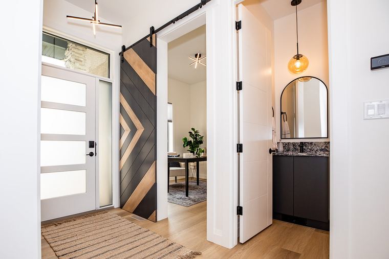Modern entry with a custom chevron barn door, contemporary lighting and an adjacent powder room with dark cabinetry.