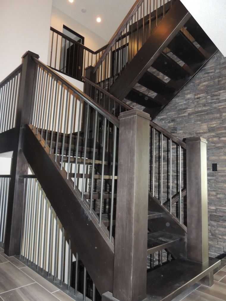 Statement open-riser staircase with dark wood framing, slim metal balusters and a floor-to-ceiling stacked-stone feature wall.
