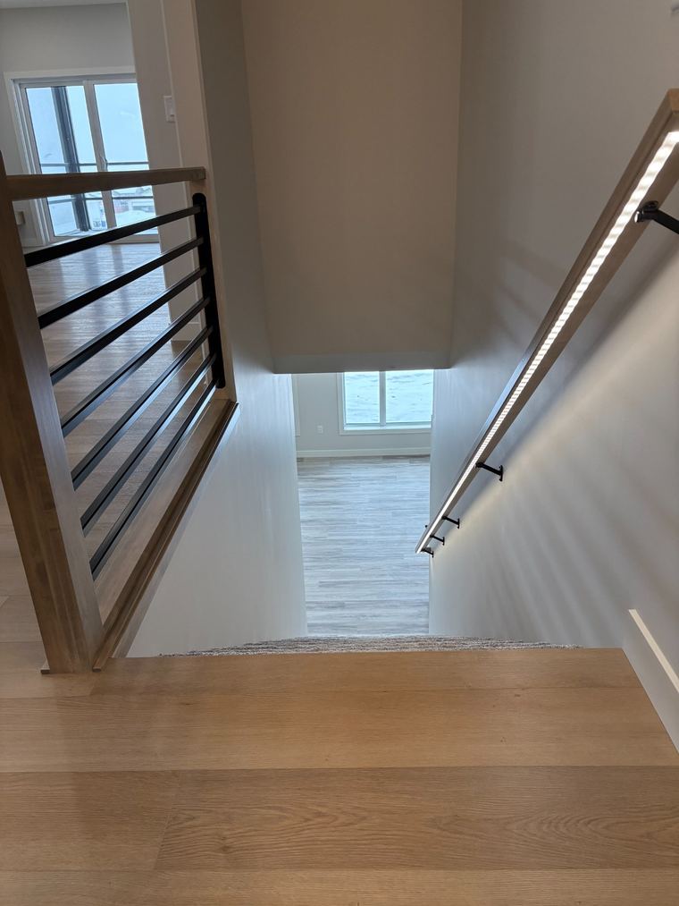 Contemporary stairwell with a wood and black metal railing, carpeted stairs and integrated LED handrail lighting.