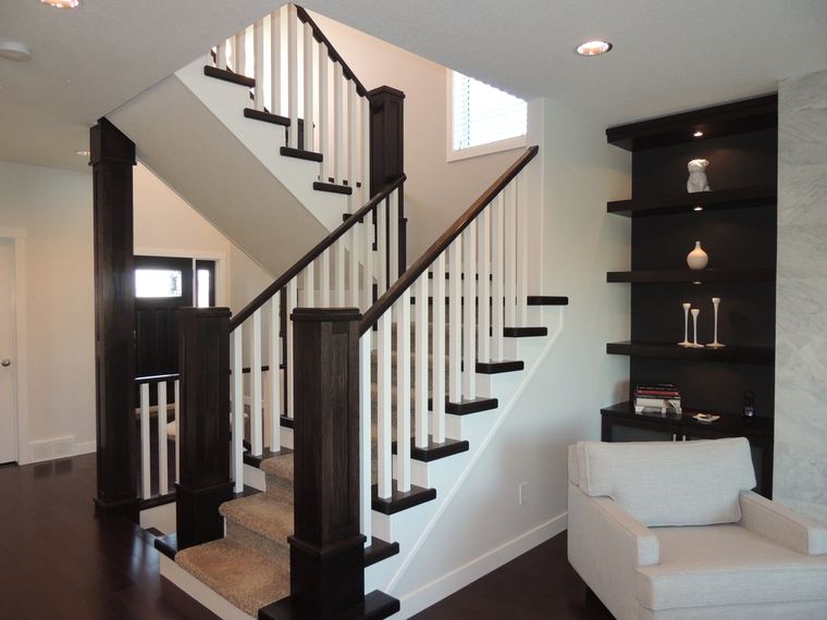 Two-tone staircase with dark wood railings, white balusters and illuminated built-in display shelving beside the living area.