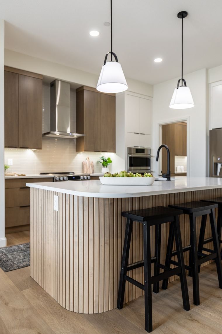 Detail view of a rounded wood-slat kitchen island with a quartz surface, black stools and modern pendant lighting.