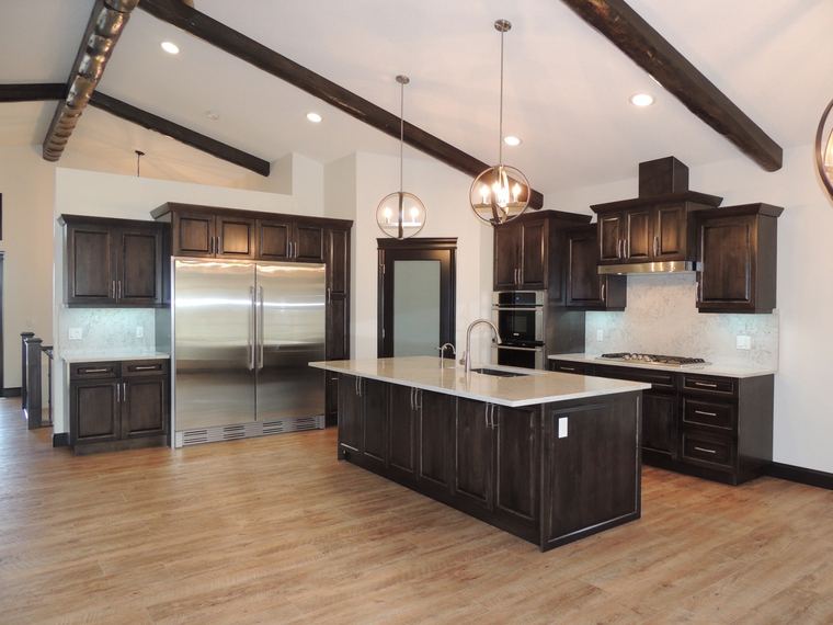 Large custom kitchen with dark wood cabinetry, exposed ceiling beams, an oversized island and commercial-style refrigeration.