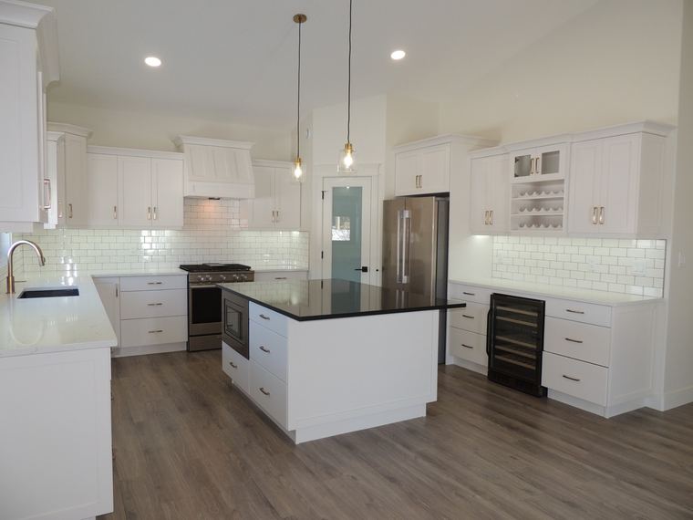 Bright white kitchen with a contrasting black quartz island, integrated wine refrigerator, brass hardware and subway tile backsplash.