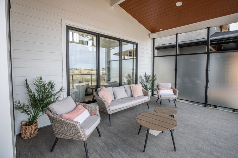 Covered outdoor living area with comfortable lounge seating, privacy screens, large patio doors and a warm wood soffit.