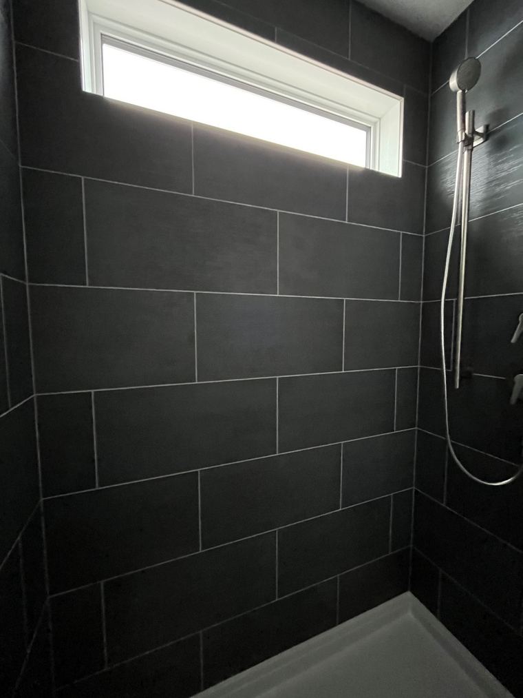 RTM home — black tiled shower with transom window and handheld fixture