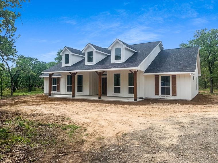 Prairie farmhouse RTM — completed exterior installed on a wooded rural property
